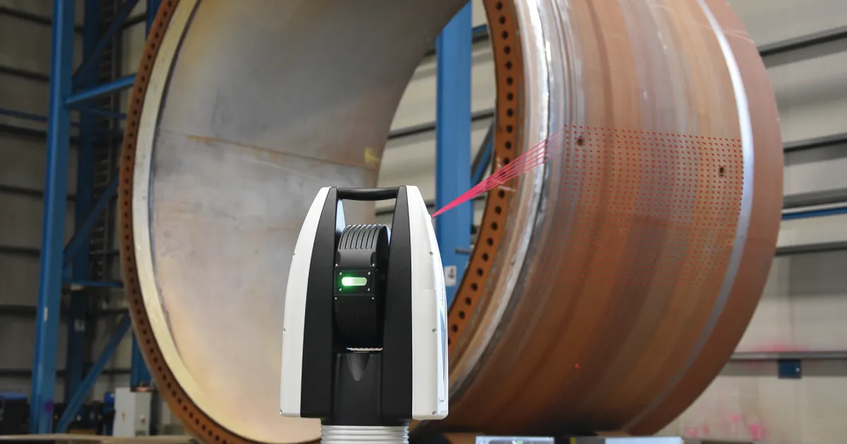 Laser tracker standing in front of a large rolled steel ring in a workshop, used for laser tracker inspection of oversized parts